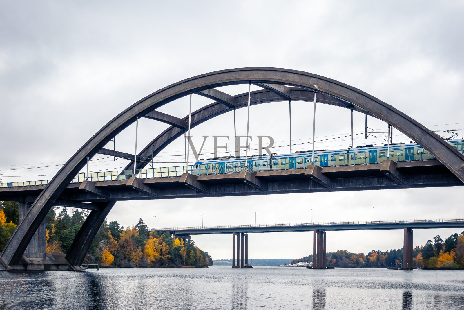 大自然的秋景景象与大型混凝土拱桥和火车跨越平静的水面。照片摄影图片