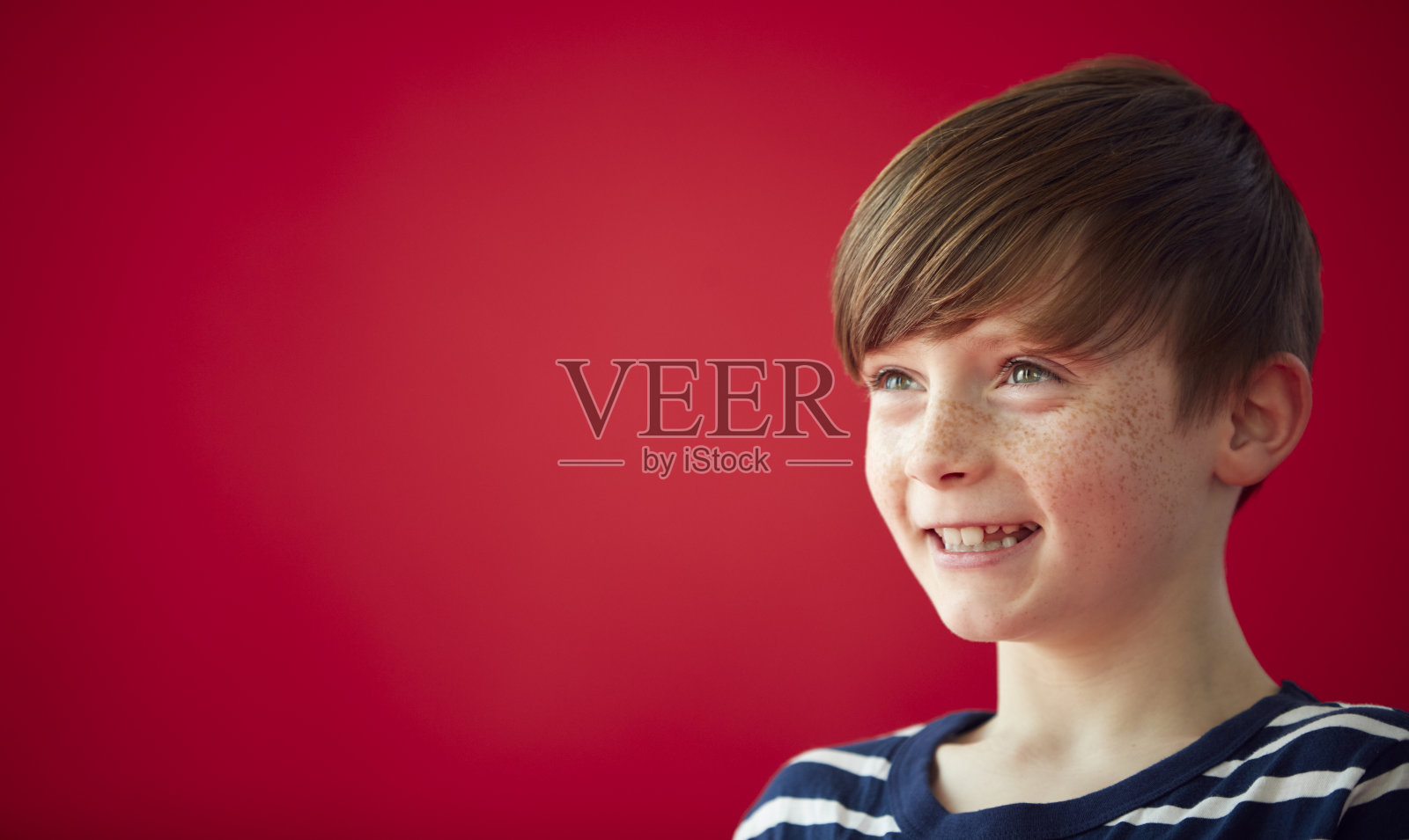 在红色工作室背景下微笑的小男孩的肖像照片摄影图片