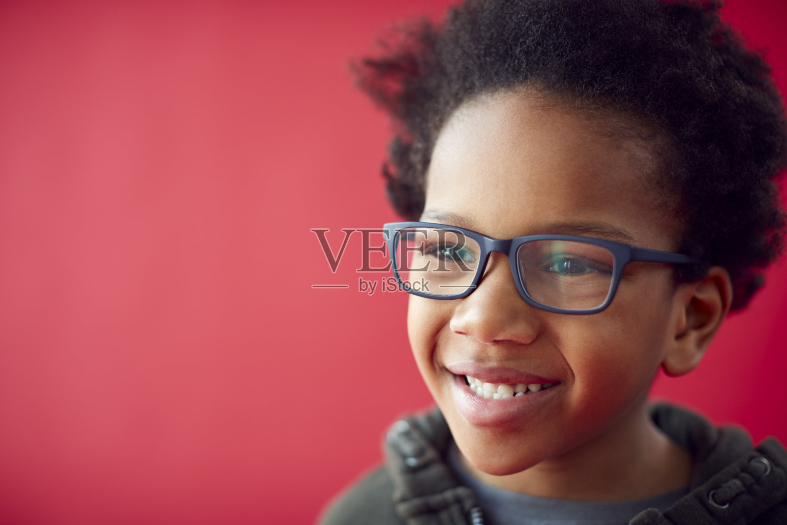 微笑的小男孩的肖像戴眼镜在红色的工作室背景照片摄影图片