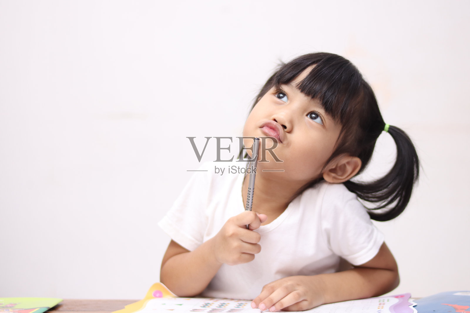 可爱的亚洲小女孩拿着笔和书，一边学习一边思考或有好主意，微笑着抬头，想象着照片摄影图片