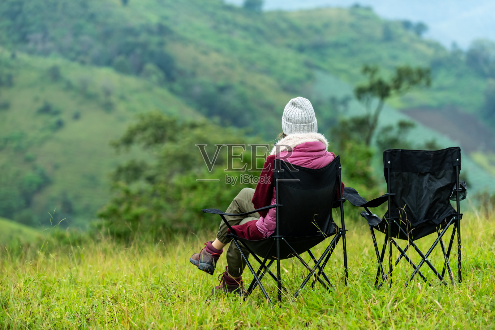 快乐年轻的亚洲女子徒步旅行者坐在户外的椅子放松在美丽的自然山草地在秋天。孤独漂亮的女孩享受与户外的生活方式度假。照片摄影图片