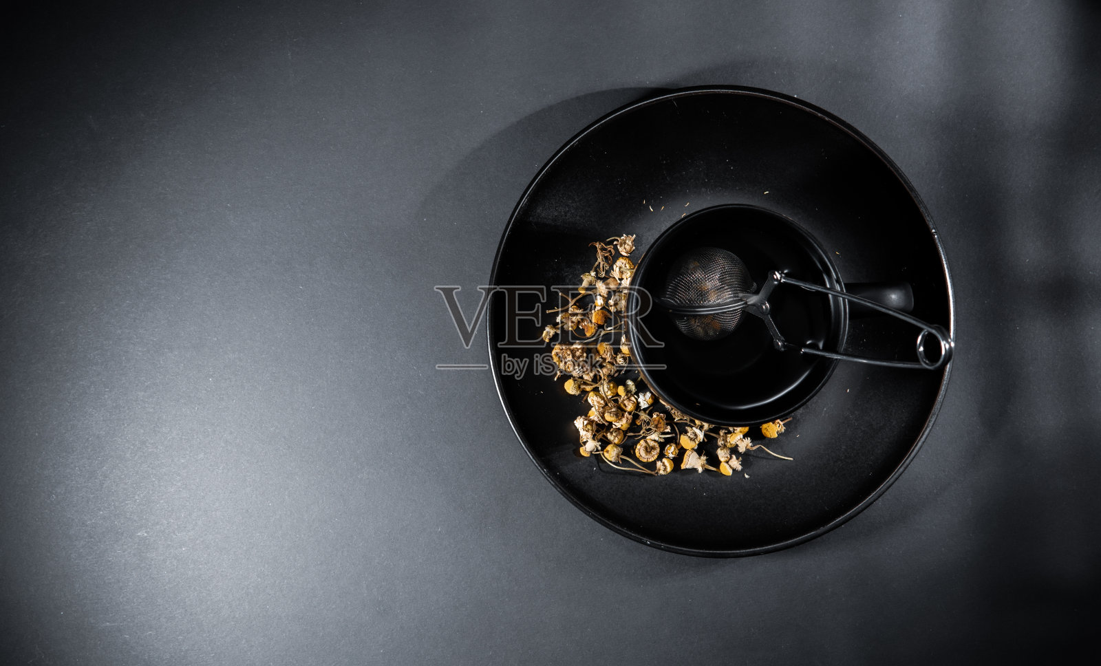 洋甘菊茶杯，有松散的干花瓣和滤网，孤立在灰黑色的背景上。照片摄影图片