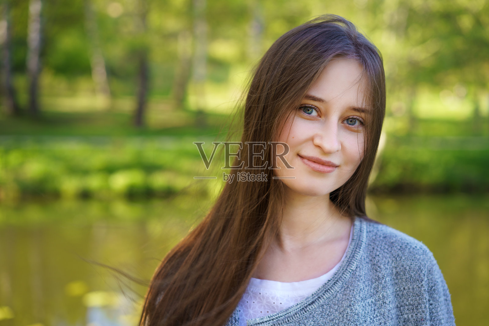 一个年轻美丽的女孩的肖像长头发，站在一个湖的背景和微笑甜甜的镜头照片摄影图片