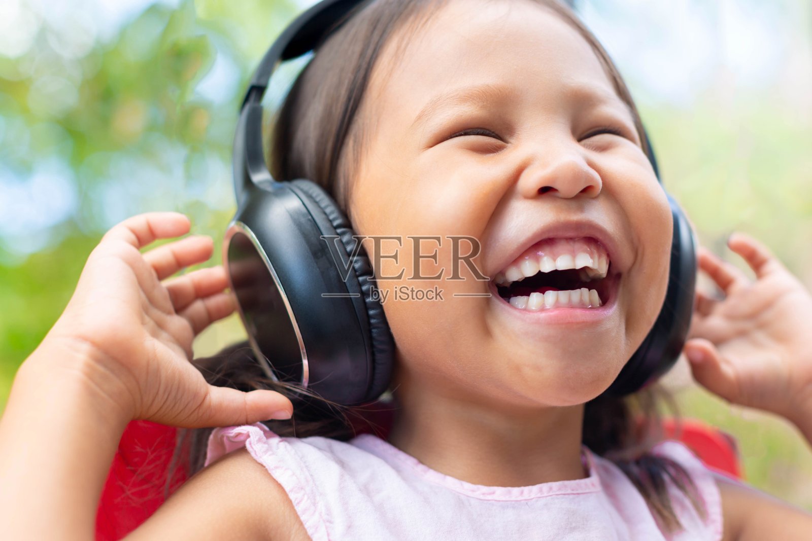 快乐的小女孩用她的耳机听音乐，带着快乐的微笑在户外。照片摄影图片