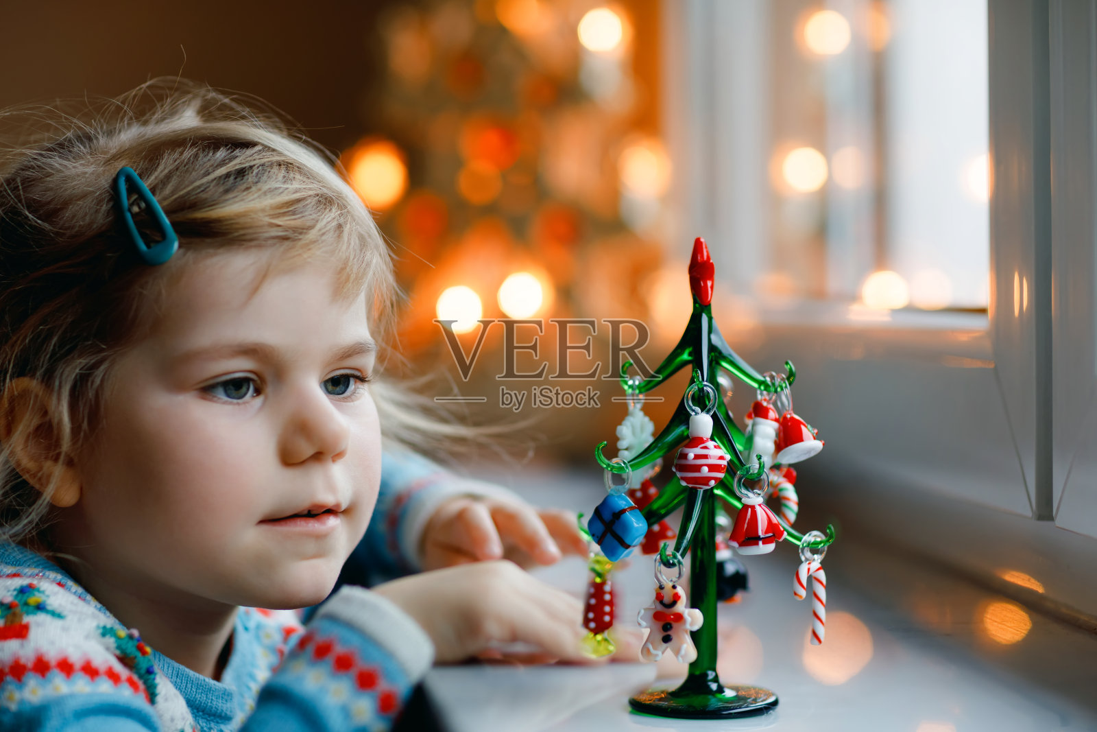 小女孩坐在窗边，用小小的圣诞玩具装饰小玻璃圣诞树。快乐健康的孩子庆祝家庭传统节日。可爱的婴儿。照片摄影图片