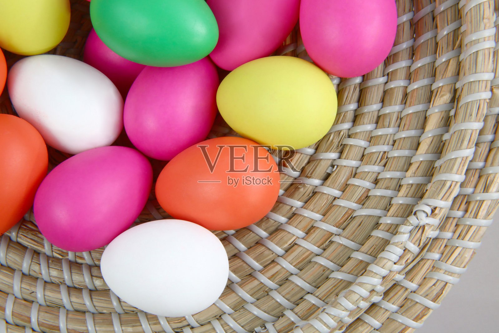 色彩鲜艳的复活节彩蛋，放在稻草篮子里，背景是灰色的。照片摄影图片