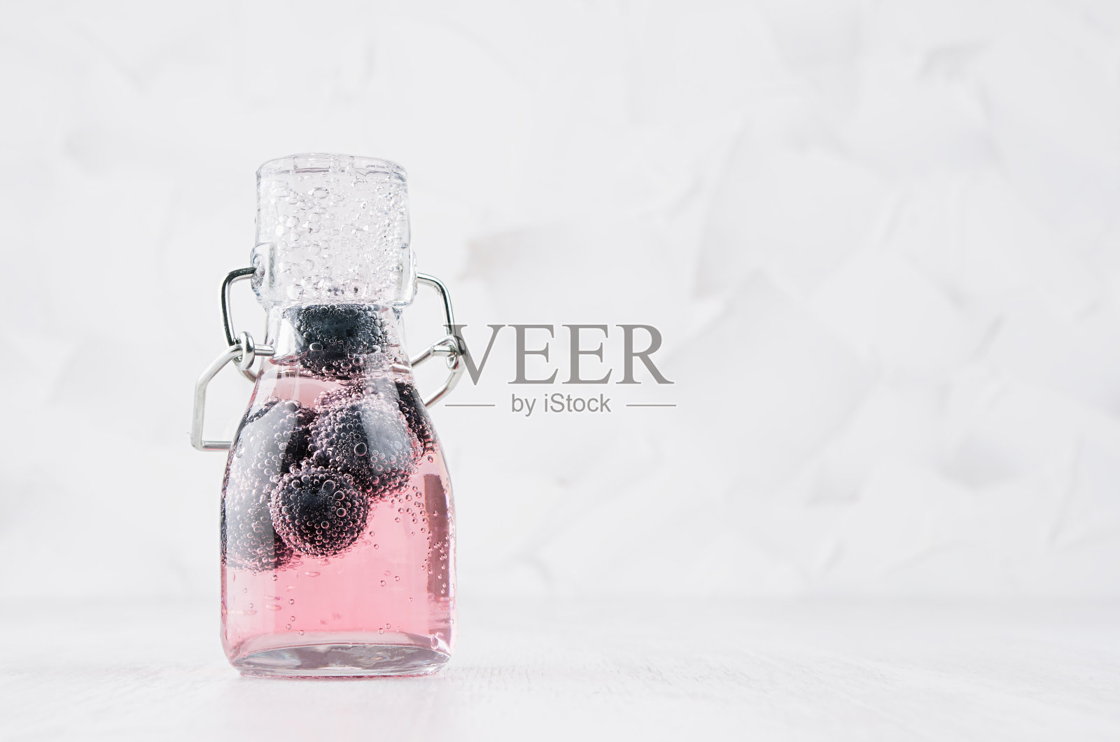 新鲜的粉红蓝莓柠檬水与浆果，苏打水在透明的轭架瓶在柔和的白色木桌，复制空间。照片摄影图片