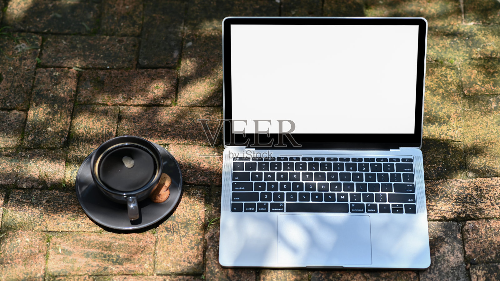 特写镜头Mockup笔记本电脑空白屏幕和咖啡在红砖地板上的花园。照片摄影图片