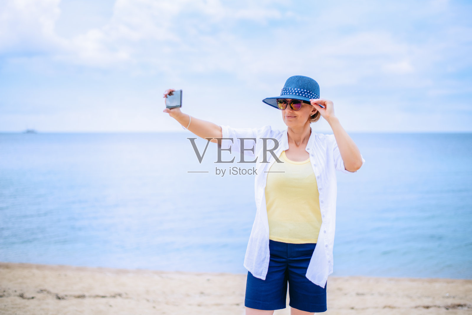 快乐成熟的女人在海边用智能手机拍照照片摄影图片