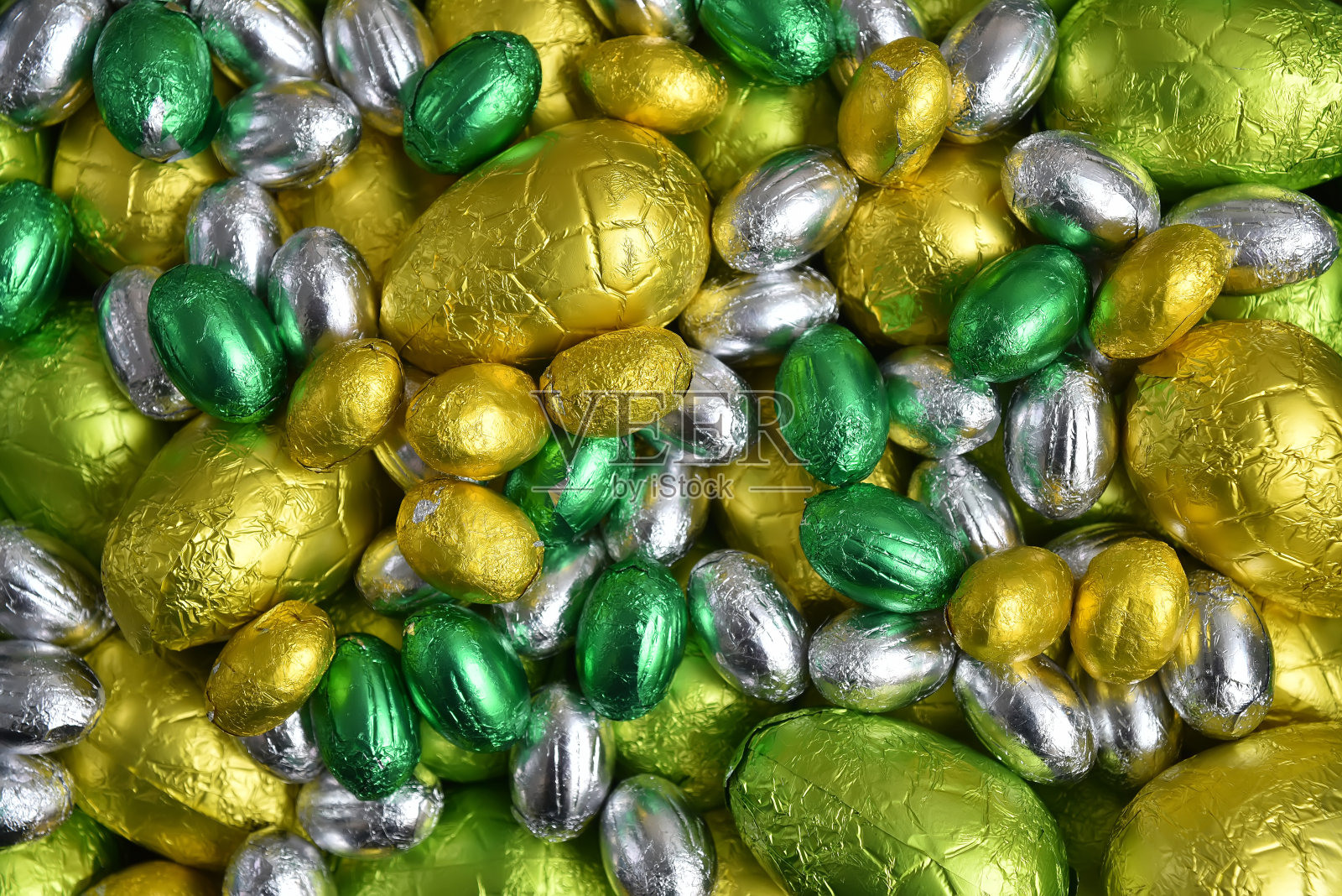 大的和小的黄色，金色，绿色，酸橙绿和银色春季颜色的巧克力包裹复活节彩蛋，在黑色的背景下。照片摄影图片