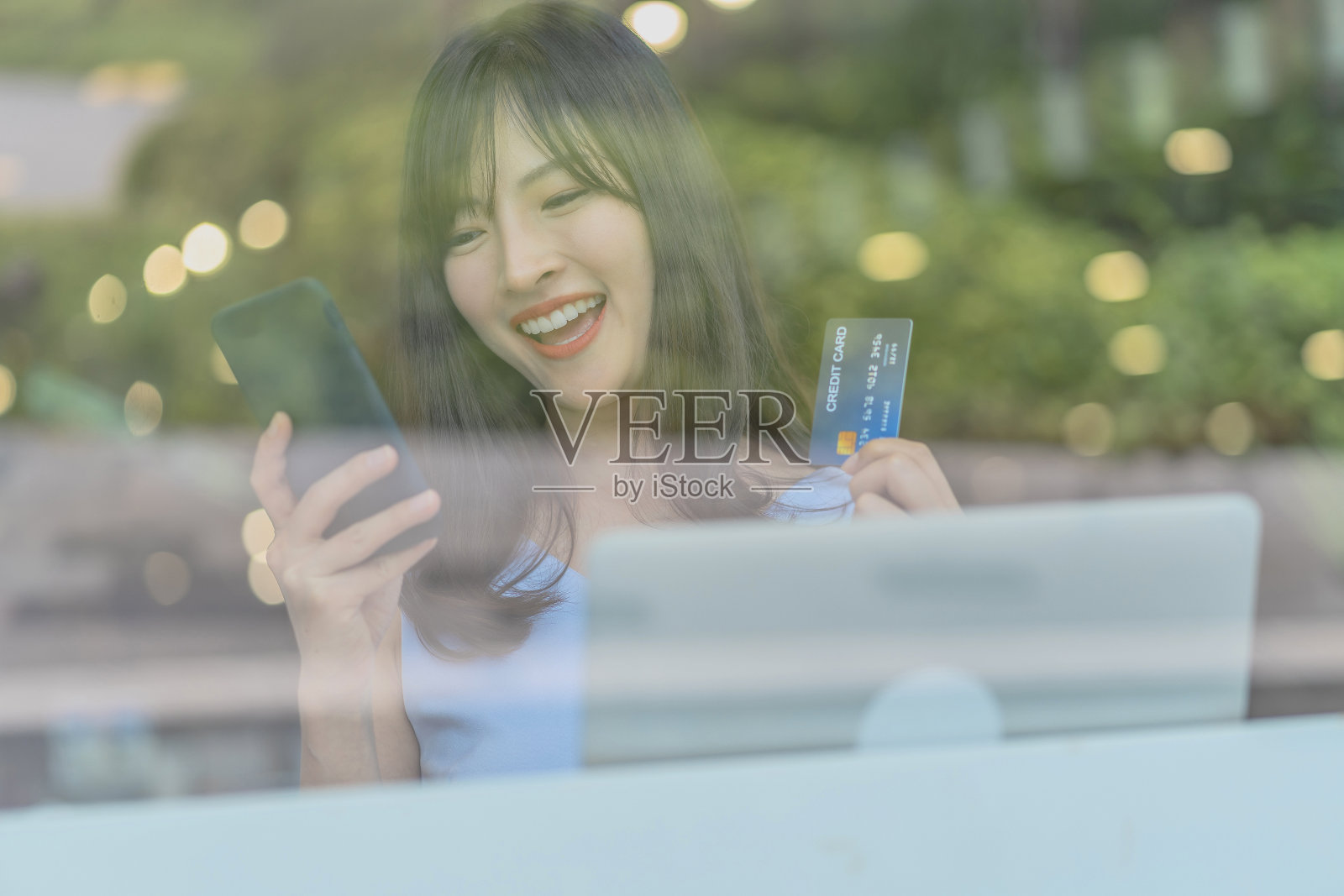 亚洲妇女使用信用卡与手机在现代咖啡店网上购物，科技钱钱包和网上支付概念，信用卡模型照片摄影图片