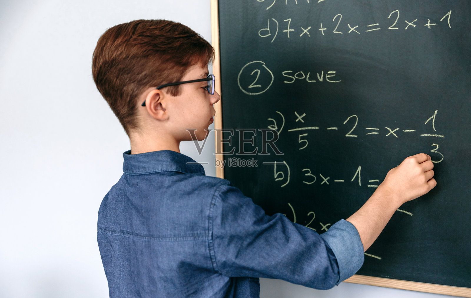 男孩在黑板上做数学题照片摄影图片