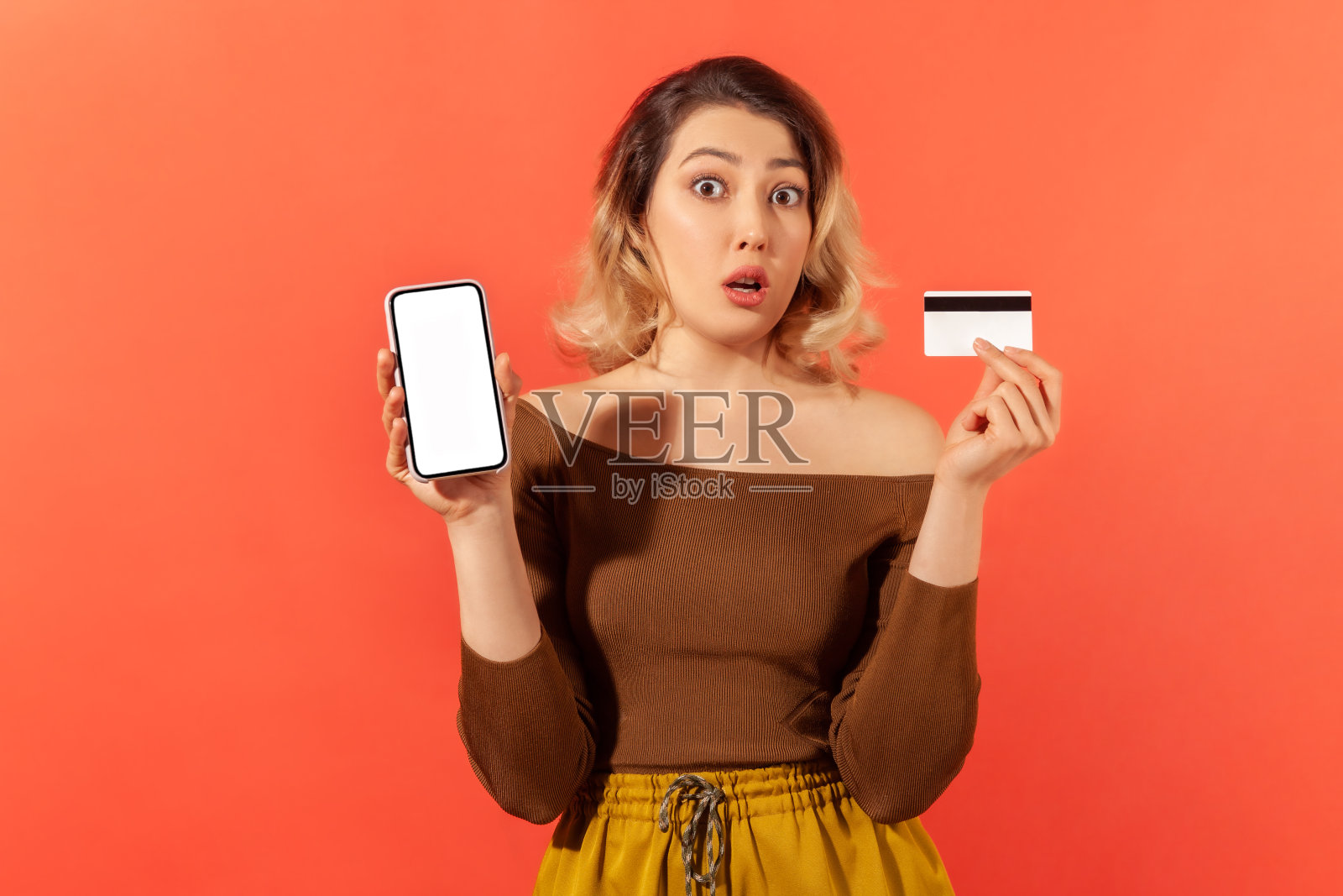 震惊的女子展示并拿着空屏幕的智能手机和信用卡，惊讶于网上信贷，网上银行照片摄影图片