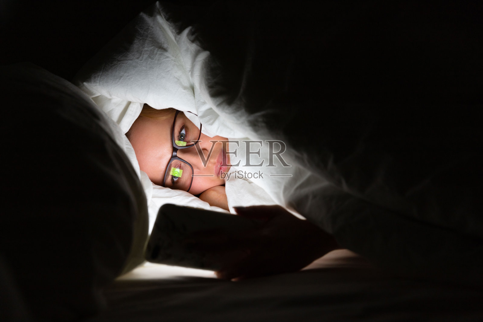 女人深夜躺在床上用手机，睡不着。失眠，无手机恐惧症，睡眠障碍。照片摄影图片