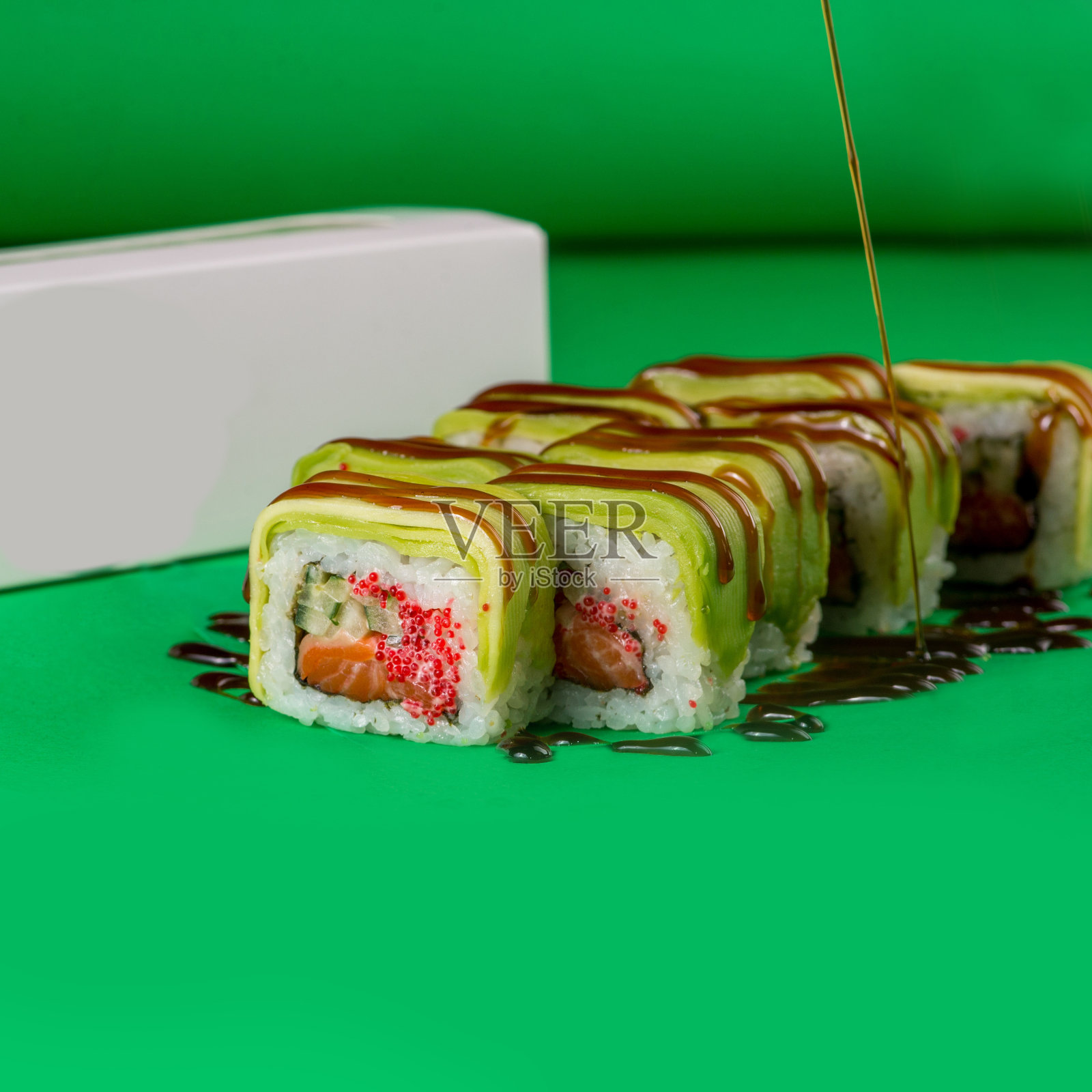 绿色背景上的鳄梨和奶油芝士寿司。特写镜头。洒上红烧酱的寿司照片摄影图片