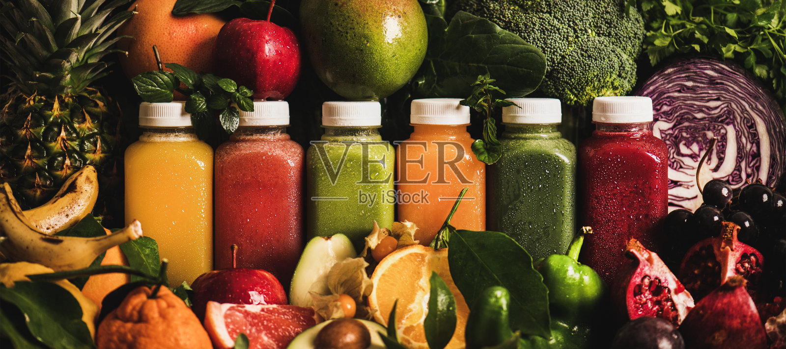 五颜六色的果汁在瓶子与水果，蔬菜和绿色周围照片摄影图片