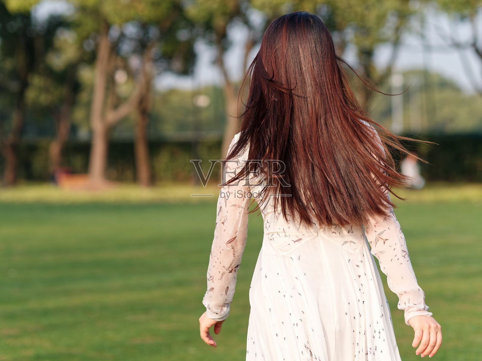 在阳光明媚的日子里，美丽的中国年轻女子穿着白色连衣裙，她的黑色长发在奔跑。照片摄影图片