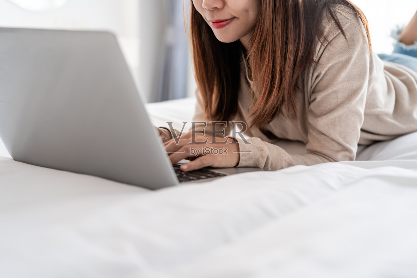 年轻女子躺在卧室的床上，在家里使用笔记本电脑照片摄影图片