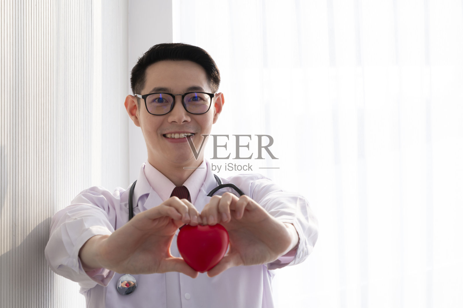 医院里拿着一颗红心的专业医生。年轻男医生拿着一只红心做成心形的手。医疗保健和医疗理念-红心男医生。照片摄影图片