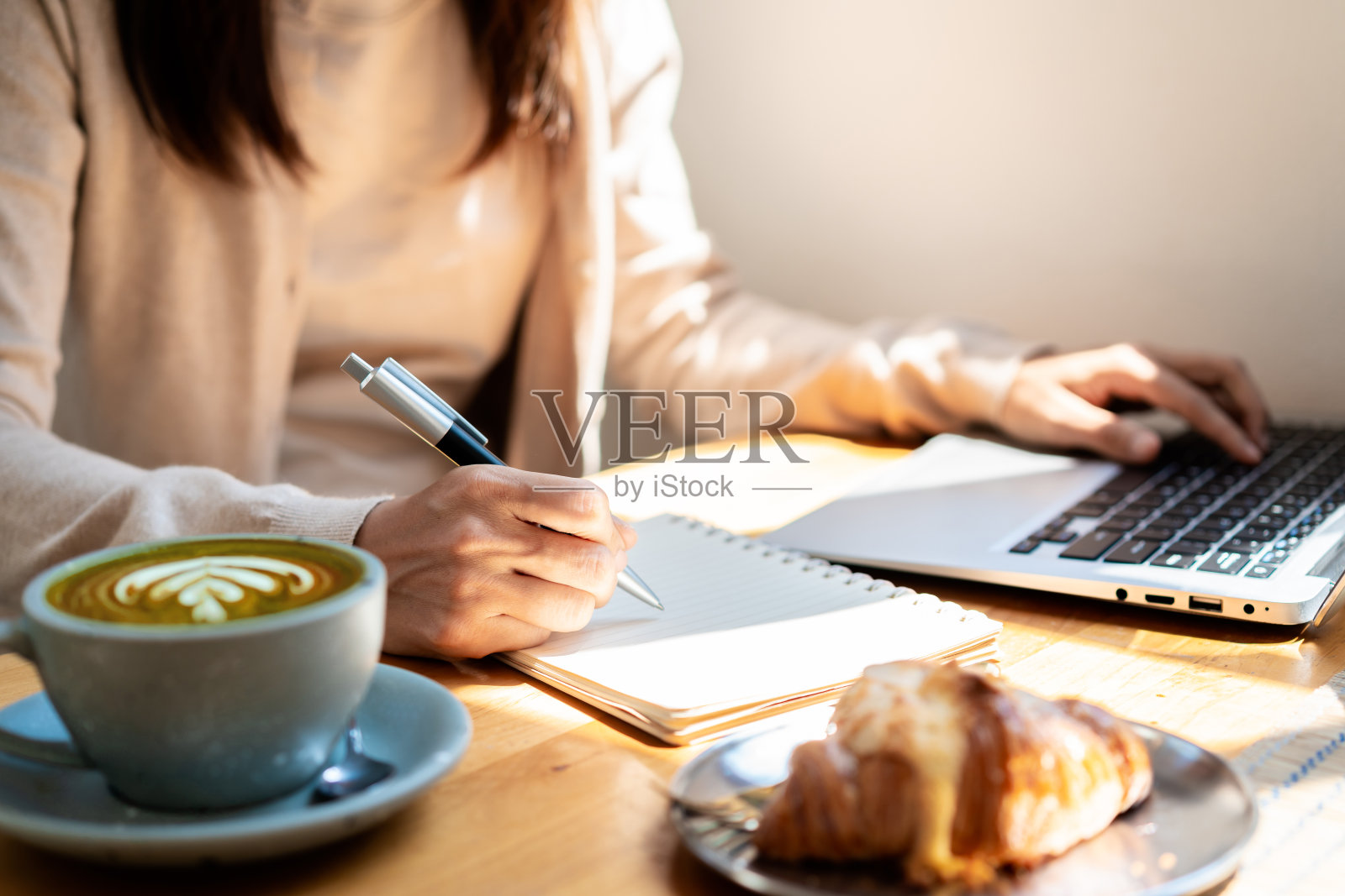 年轻女子拿着一杯咖啡坐在咖啡店里用笔记本电脑工作照片摄影图片