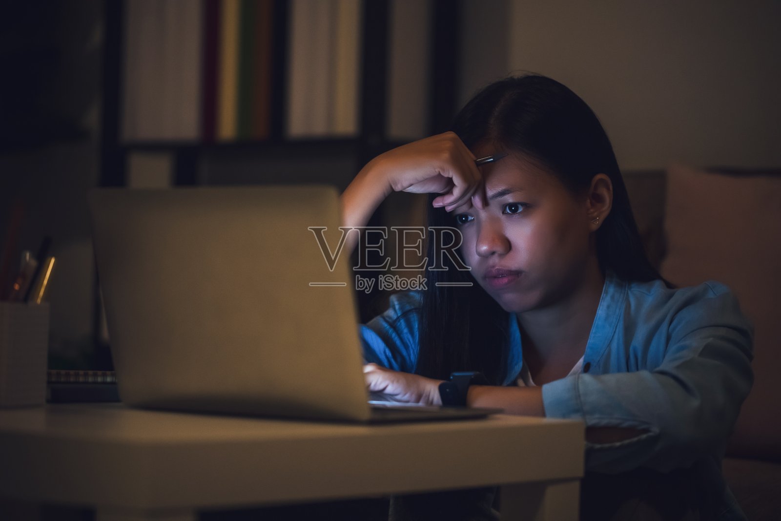 亚洲女学生或女商人工作到深夜。在漆黑的房间里，坐在书桌前，拿着笔记本电脑，注意力集中，昏昏欲睡。人们努力工作和倦怠的概念。照片摄影图片