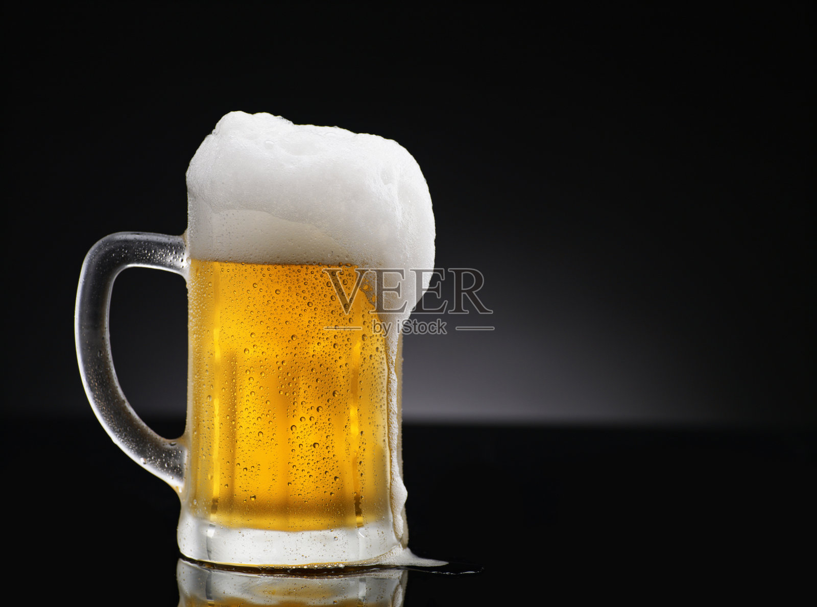 冰镇的啤酒杯，上面覆盖着冰和水滴-凝结。站在黑色的桌子上，黑色的背景。照片摄影图片