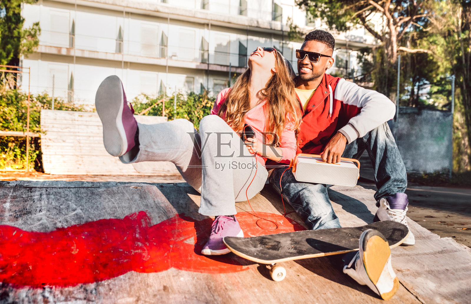 多种族的夫妇有乐趣在滑板公园与音乐扬声器-城市生活方式概念与真诚的人在户外的爱情故事开始-阳光明媚的一天与温暖的对比过滤的音调照片摄影图片