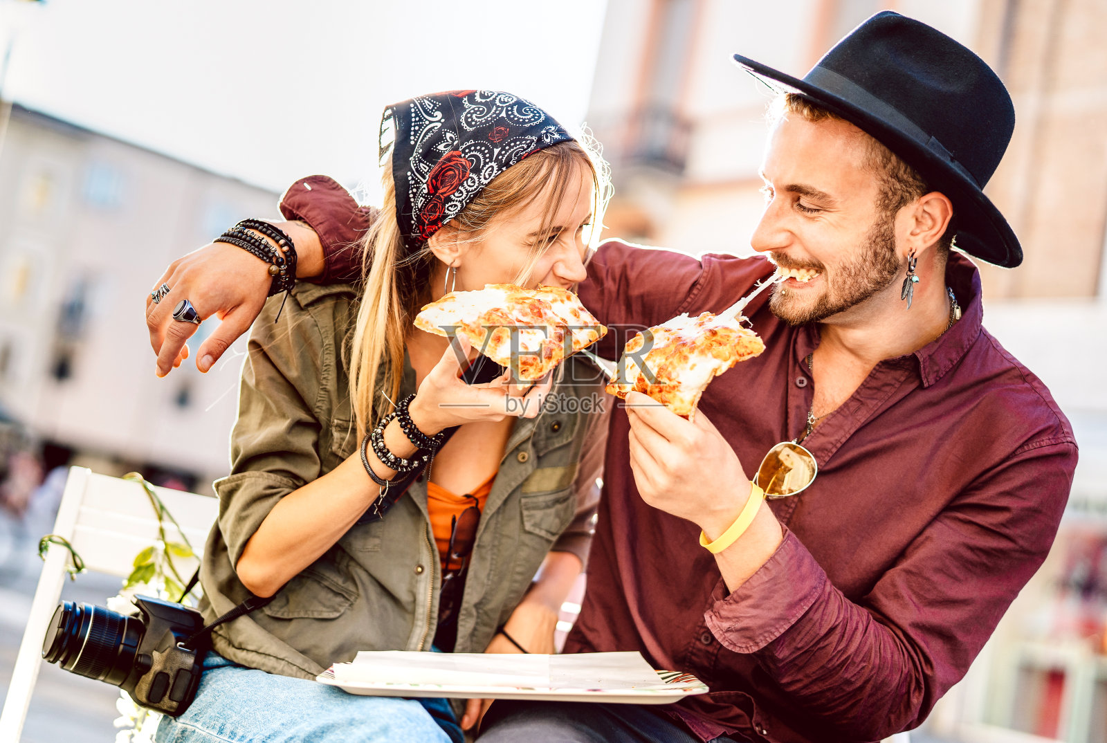 年轻的潮人夫妇在户外的酒吧餐厅吃披萨-快乐的关系概念与千禧一代的男朋友和女朋友在一起有乐趣的时刻-明亮生动的滤镜与焦点在脸上照片摄影图片