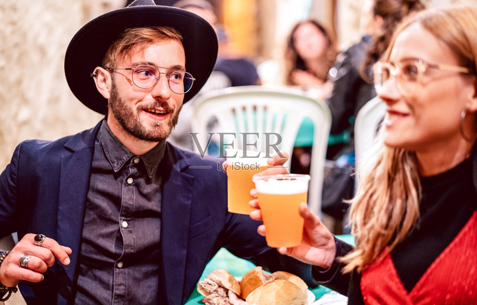 年轻的夫妇在街头食品节上祝酒啤酒杯-饮料生活风格概念与朋友一起在啤酒厂酒吧的快乐时光-明亮生动的滤镜与关注的家伙与帽子照片摄影图片