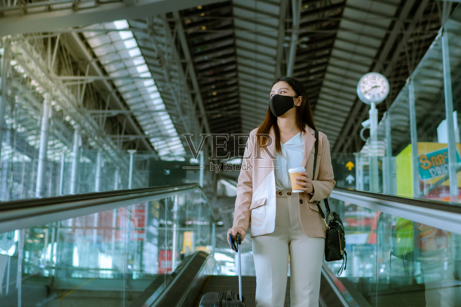 在机场使用自动扶梯时戴口罩的亚洲女商人。照片摄影图片