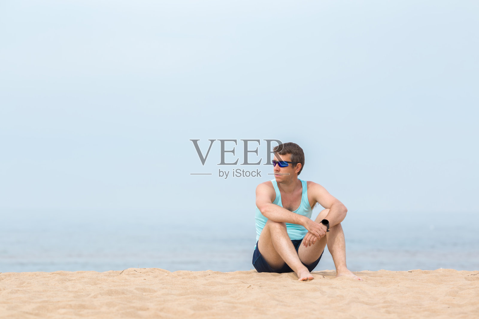 在温暖阳光明媚的早晨，一个年轻人独自坐在沙滩上，望着远处平静的海滩。对生活的想法。宁静的自然氛围。文本、引用或语录的空地方。照片摄影图片