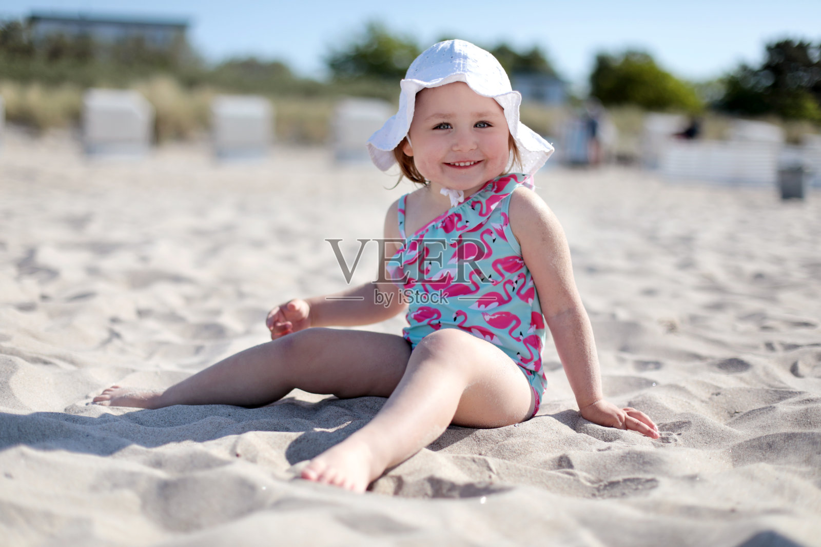 快乐的小女孩坐在白色的沙滩上照片摄影图片