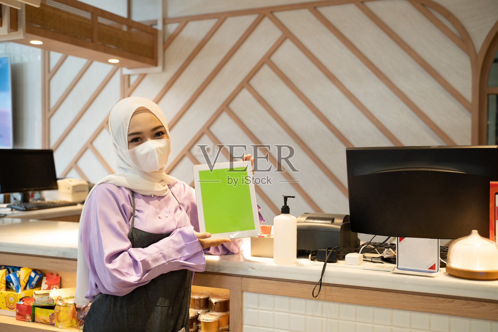 女商人戴着头巾和面具站在她的商店里，展示着空白的平板电脑照片摄影图片