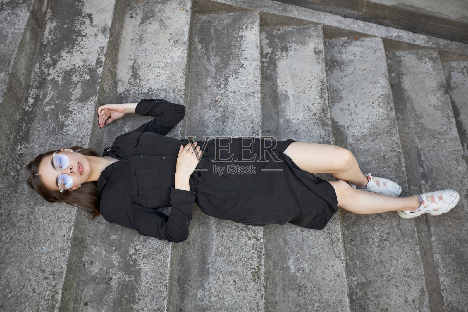 性感的黑发女人化妆穿着黑色时髦的连衣裙躺在水泥楼梯上照片摄影图片