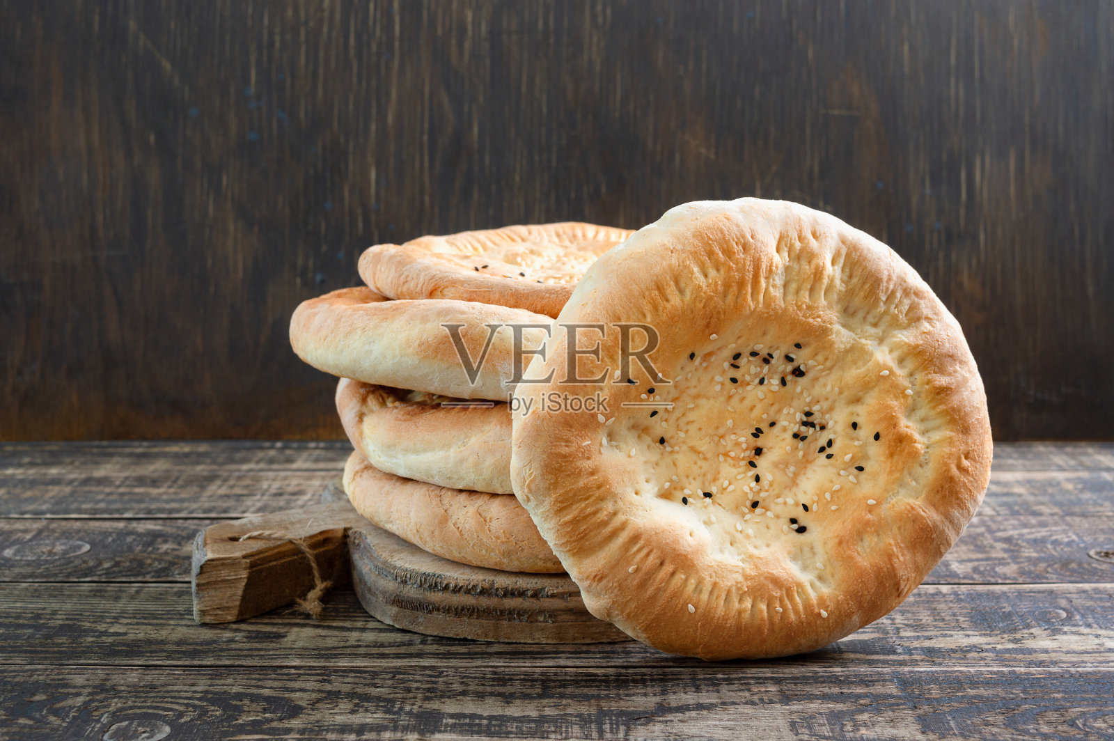 木制背景上的一堆圆形的未发酵的烙饼。简单的乡村芝麻面包。照片摄影图片