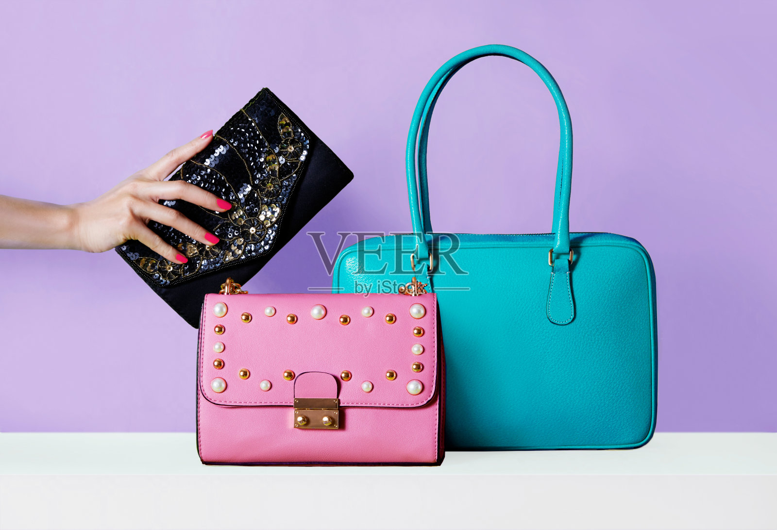 五颜六色的包包，紫色背景的钱包。女人用红色指甲拿着钱包。照片摄影图片
