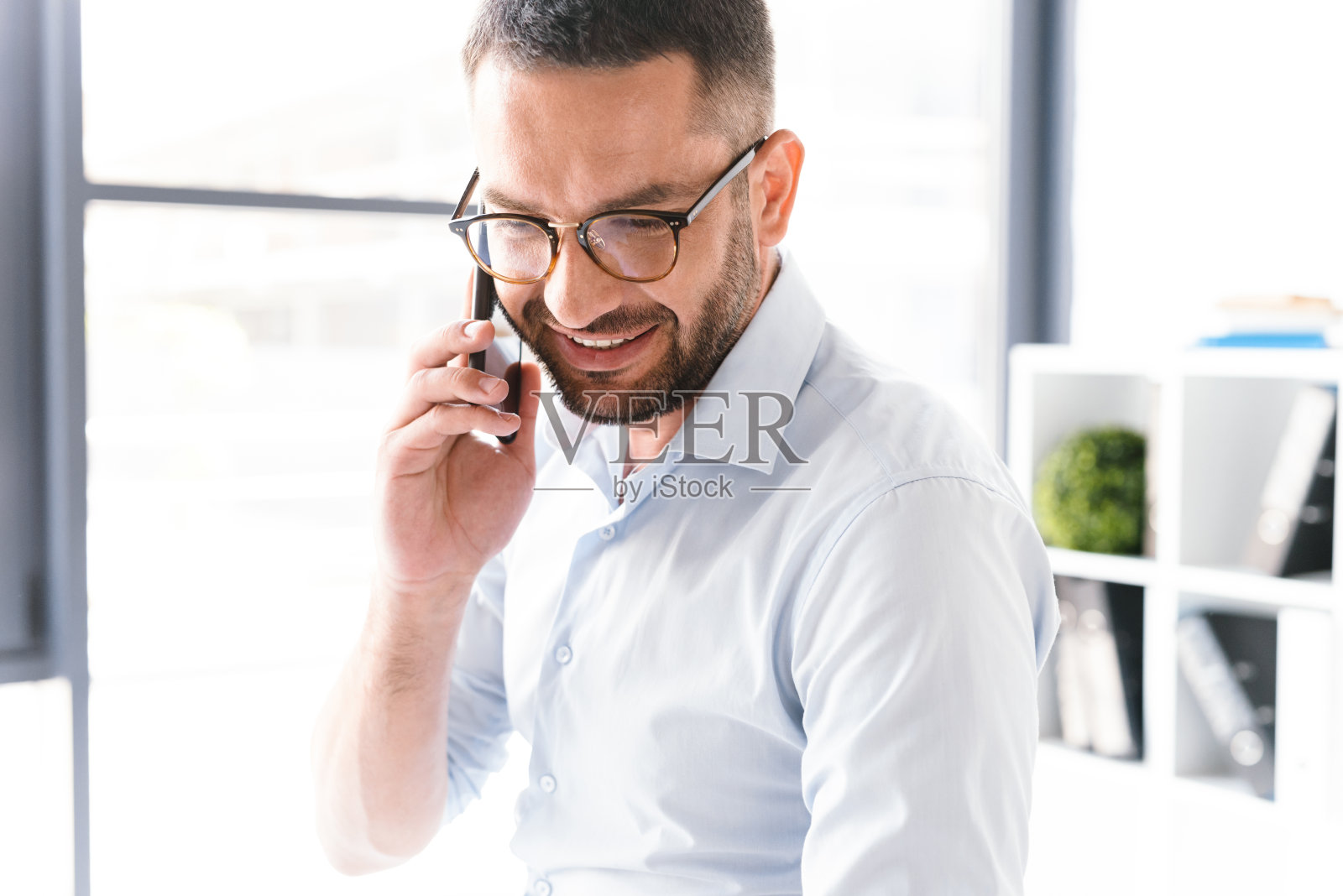这张照片的特写是一名穿着正式的大胡子男子在办公室里用黑色智能手机谈论生意照片摄影图片