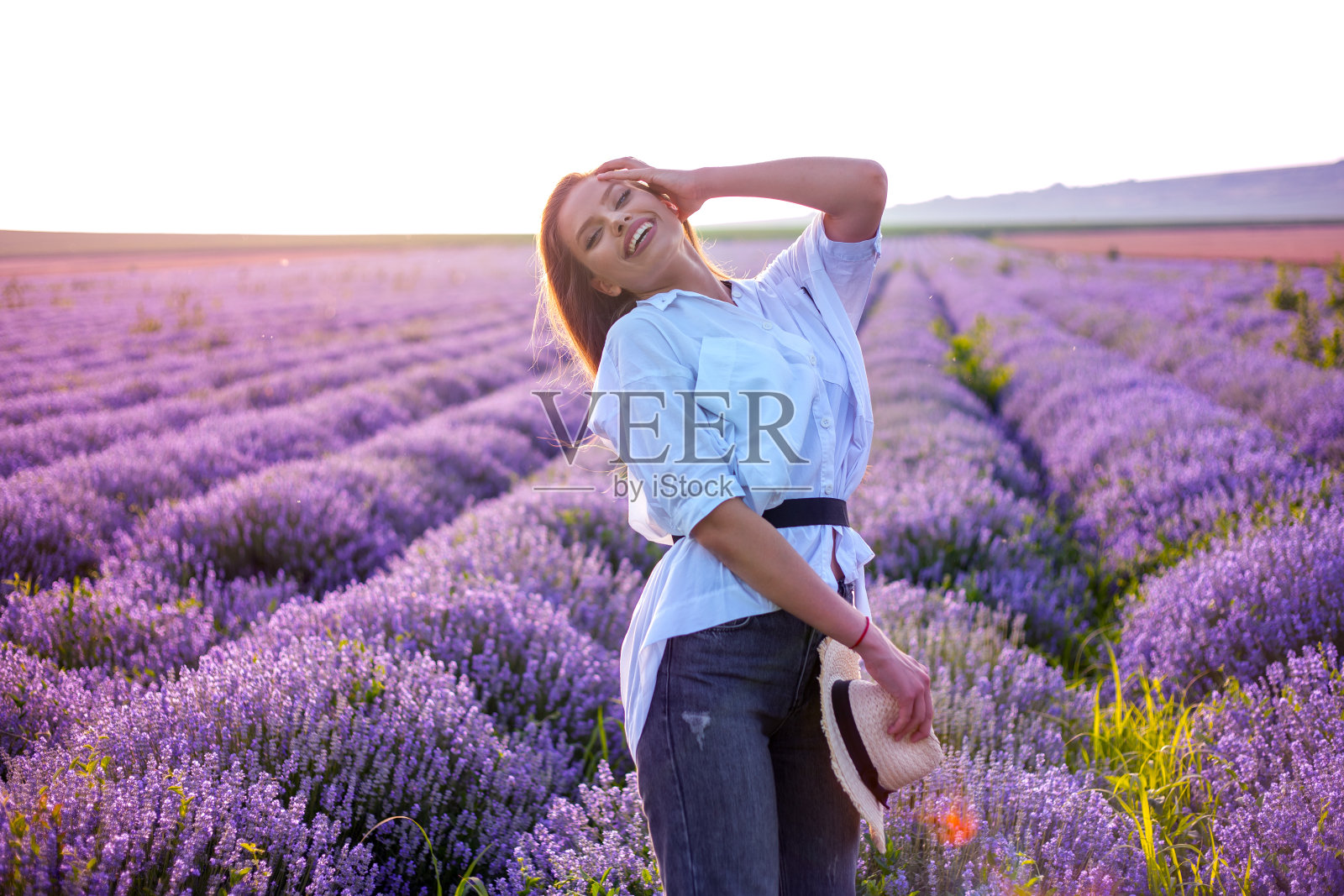 一个美丽的微笑的年轻女子的肖像与长头发在一个盛开的薰衣草田照片摄影图片