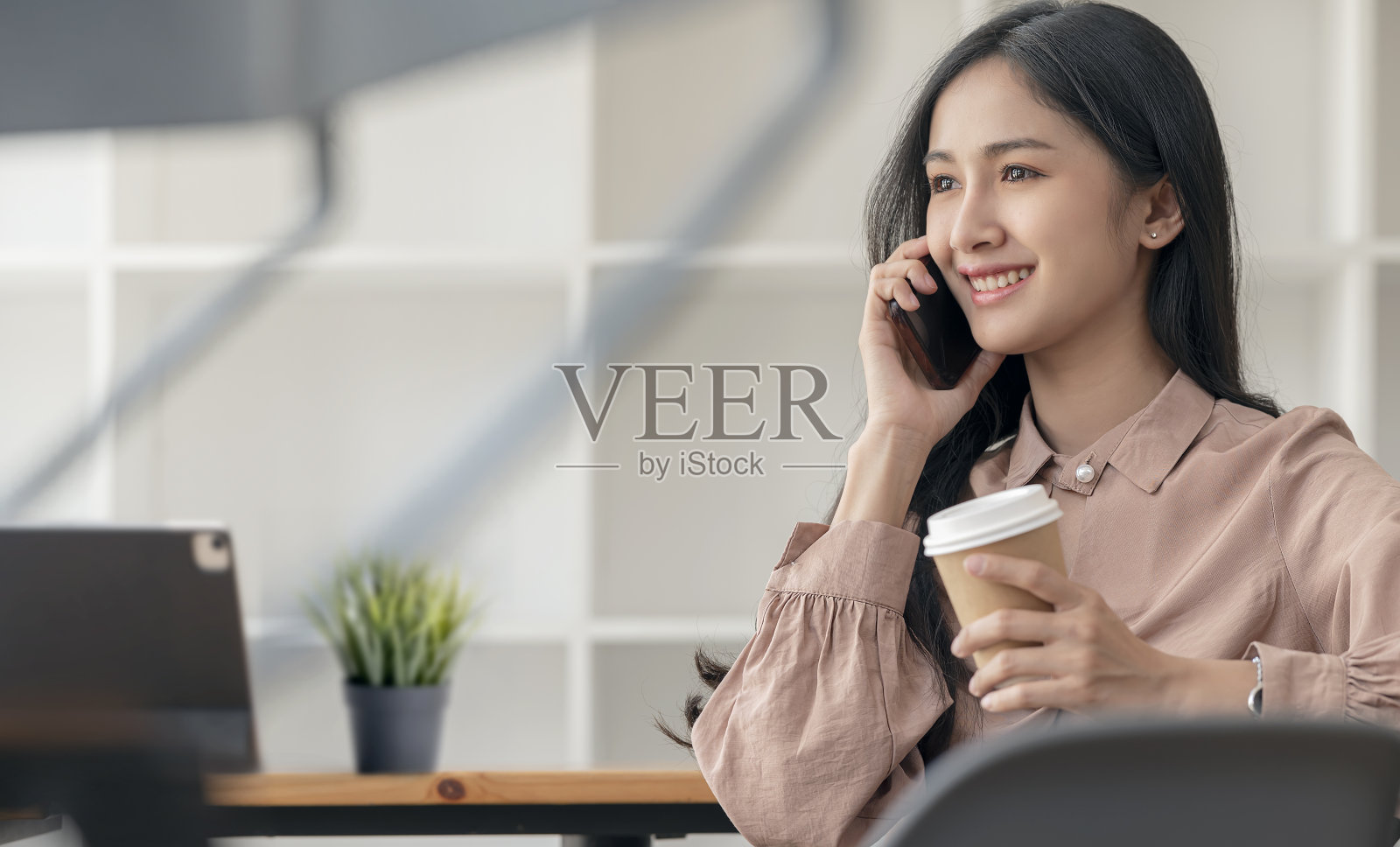 美丽的亚洲女人拿着一杯咖啡，坐在咖啡馆的桌子上使用智能手机的肖像。照片摄影图片