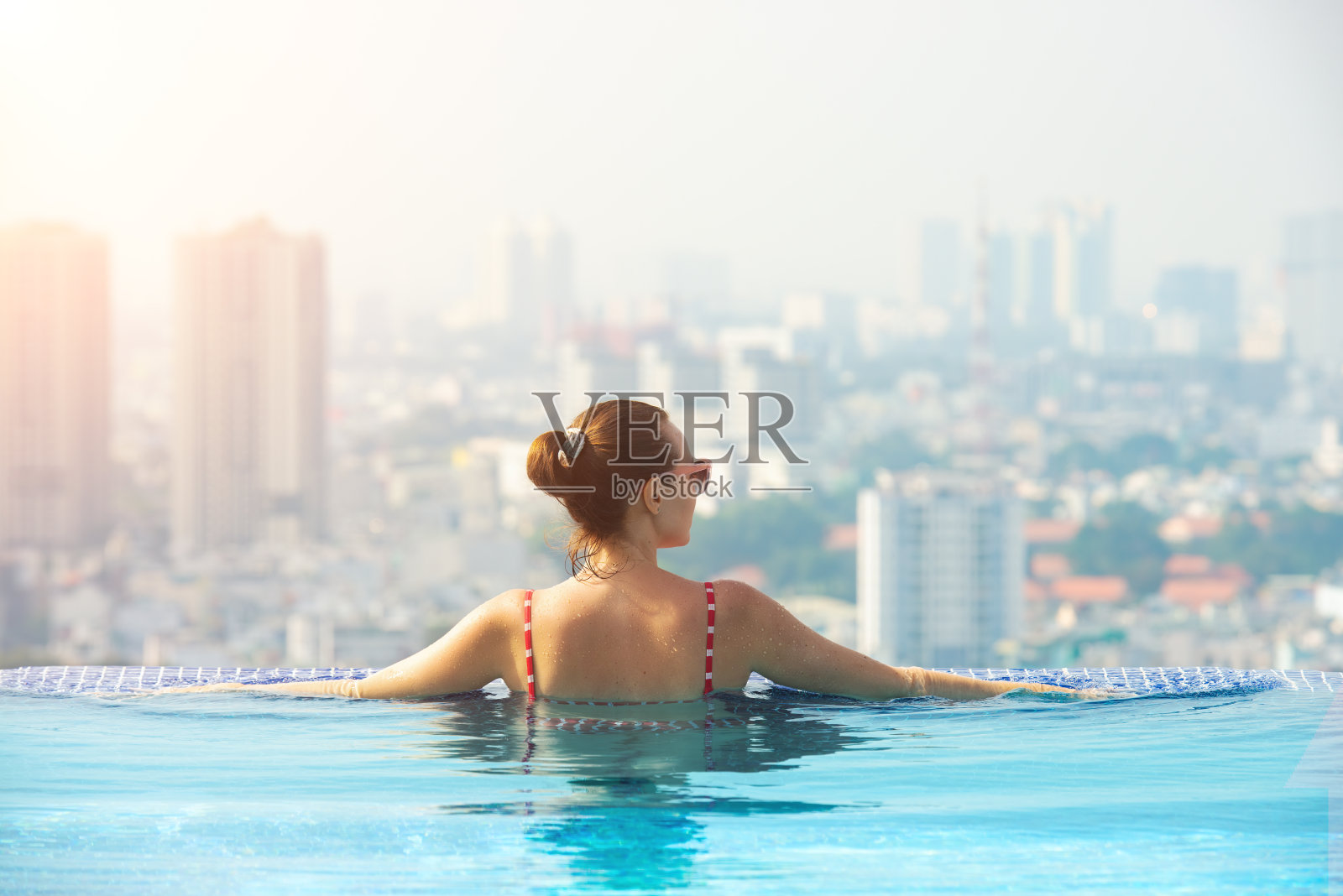 快乐的女人在以大城市为背景的酒店屋顶泳池里享受照片摄影图片