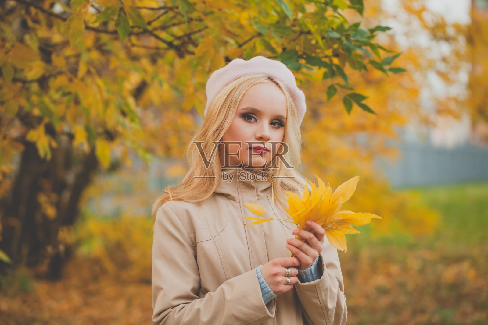 秋天的画像，漂亮的年轻女子手里拿着一片枫叶照片摄影图片