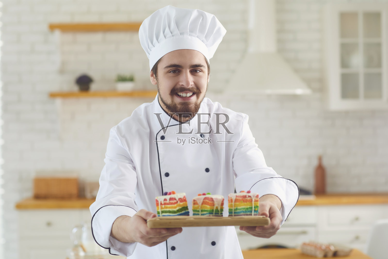 糕点师傅站在厨房的面包房，手里拿着蛋糕，脸上挂着微笑照片摄影图片