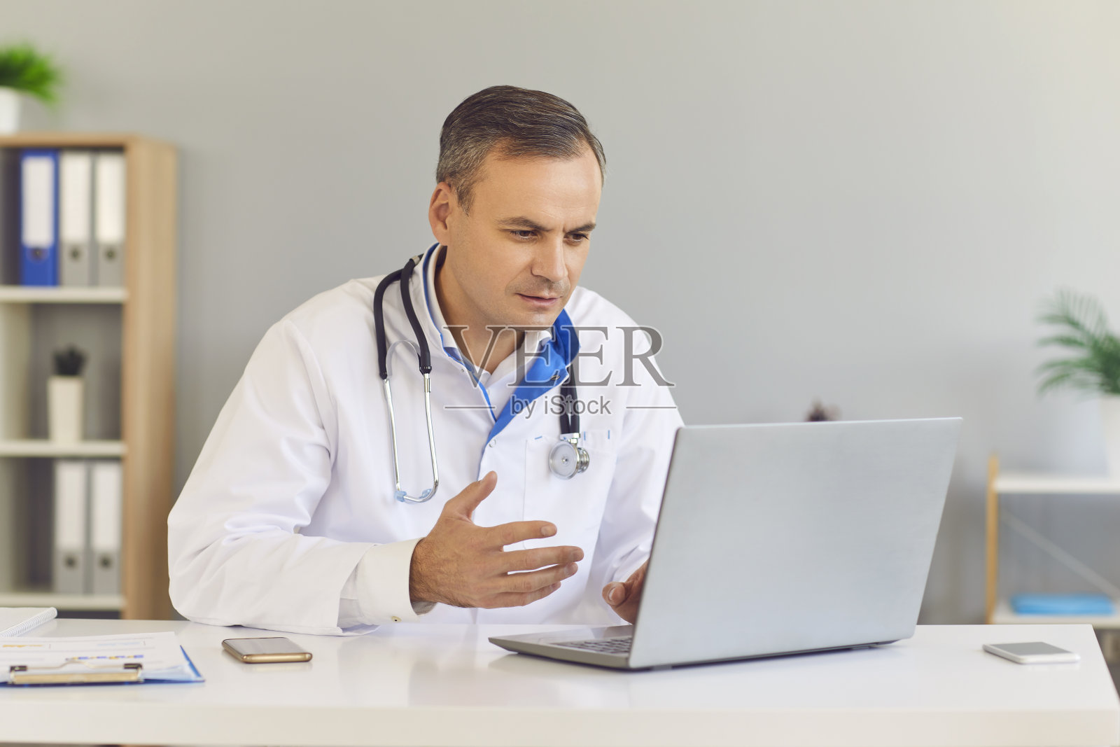 一名男性家庭医生用一台笔记本电脑为他的病人进行在线咨询。照片摄影图片