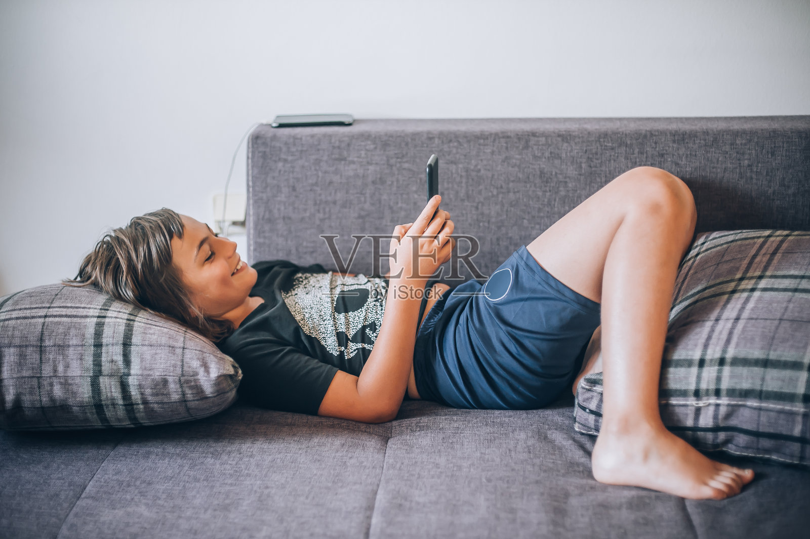 十几岁的男孩拿着智能手机查看社交媒体，躺在沙发上休息照片摄影图片