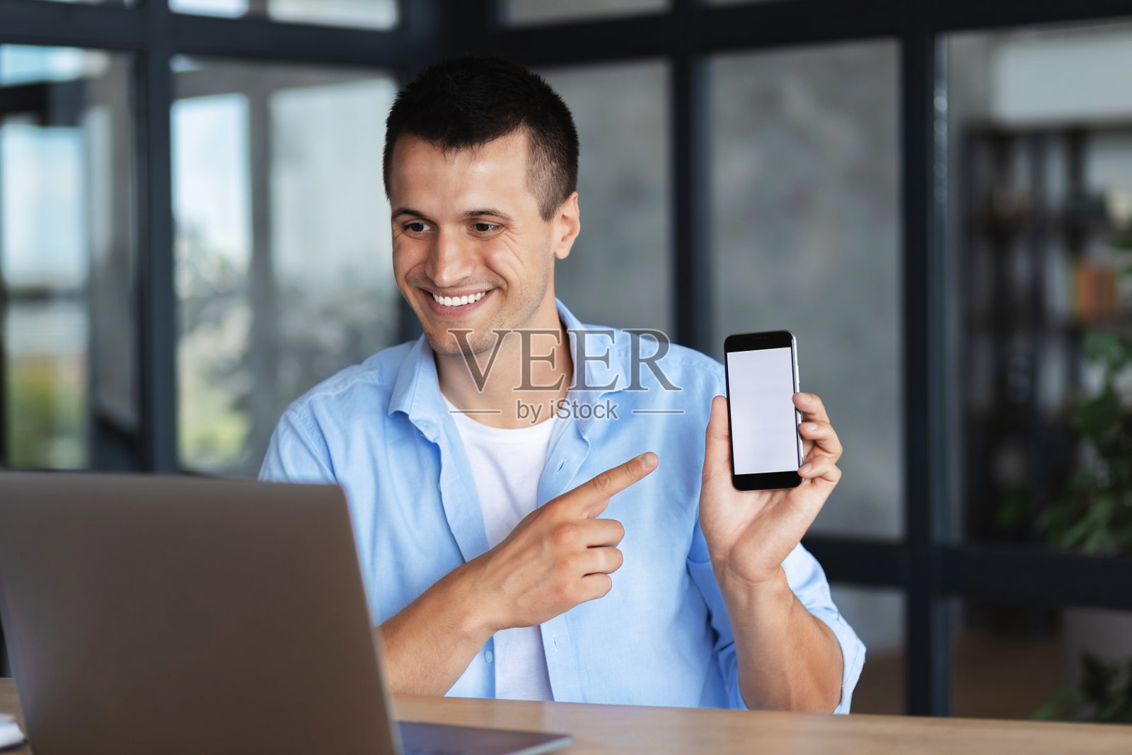 一名英俊的白人青年在笔记本电脑屏幕上展示着一个黑屏手机视频会议照片摄影图片