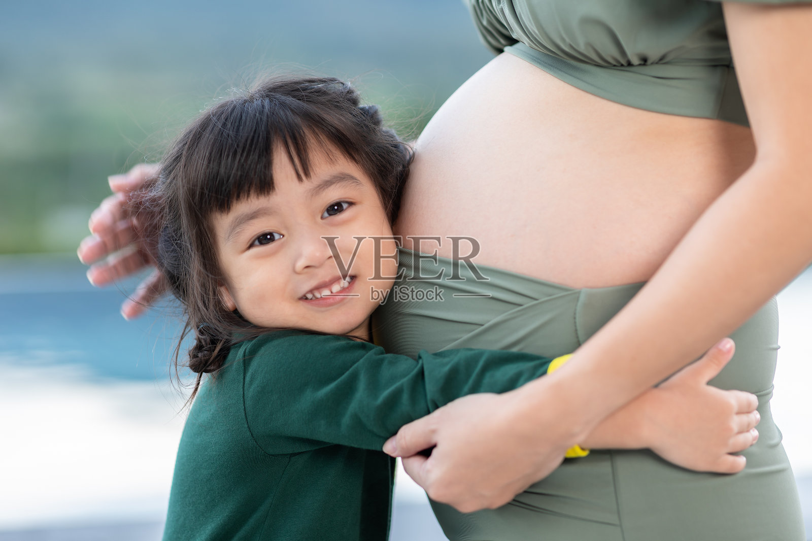 可爱的小女孩抱着孕妇的肚子，听到宝宝的声音。可爱的小女孩爱着，等待着她妈妈肚子里刚出生的妹妹。开心的孩子笑着妈妈怀孕的肚子照片摄影图片