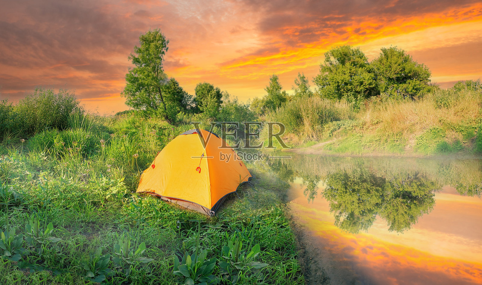 在日落的天空下，河岸上的绿色草地上的橙色帐篷照片摄影图片