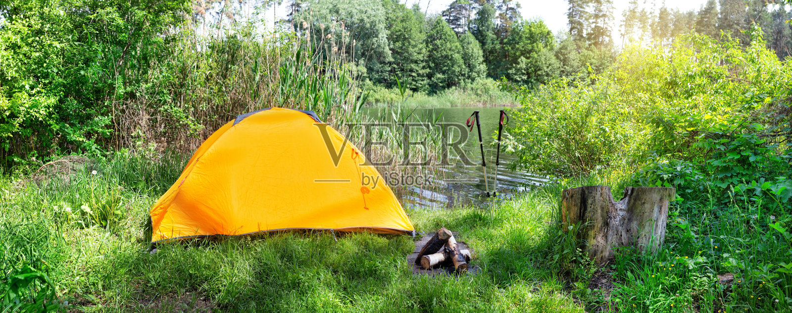 河流背景上的橙色帐篷和夏天的登山杆照片摄影图片