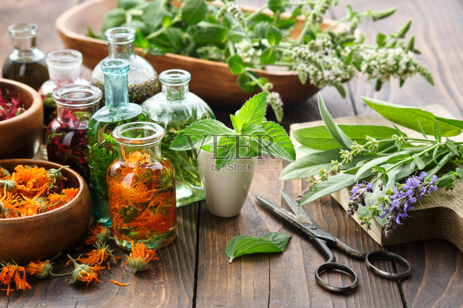 木桌上摆放着金盏花、薄荷、鼠尾草、牛至、愈合植物和药草等精油或药草和浆果的瓶子。替代医学。照片摄影图片