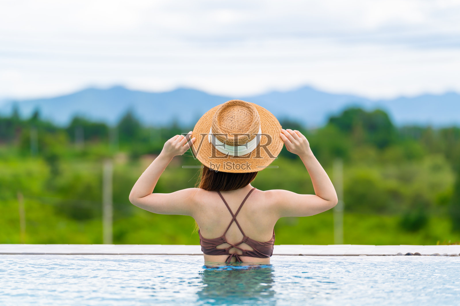 后视镜的女人在豪华酒店热带度假村游泳池放松太阳帽。女性喜欢在户外过暑假。照片摄影图片